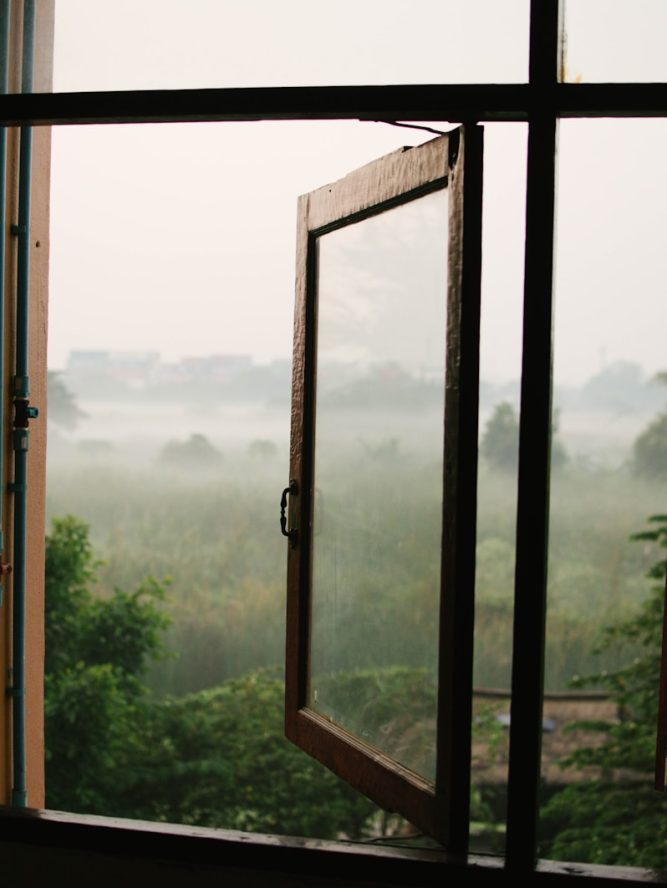 an open window with a view of a foggy field